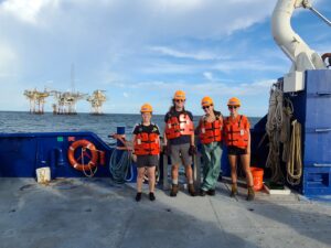 An oil platform serves as the backdrop for this photo opp of our student crew members on the "day shift". From left to right: Maya, "Young" Benjamin, Abby, and Jill.